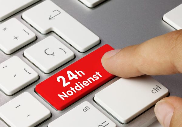 Finger drückt eine rote Taste mit der Aufschrift 24h Notdienst